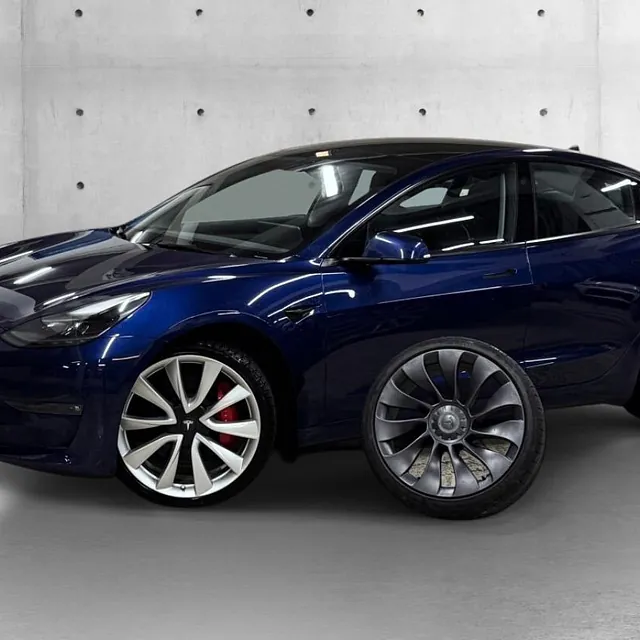 Blå Tesla Model 3 med store aluminiumsfelger, avbildet i studio med blank lakk og sporty uttrykk